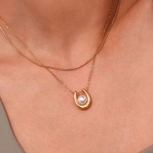Close-up of a U-shaped horseshoe pendant necklace with white pearl and 18K gold finish