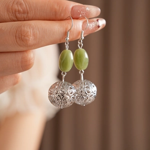 Close-up of green resin hollow pendant earrings worn by a model in warm light