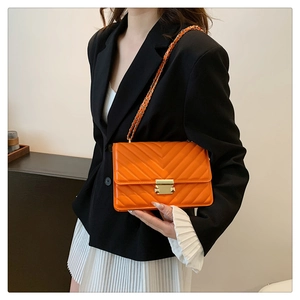Orange V-quilted shoulder bag with gold chain strap worn over a black blazer and white skirt