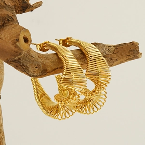 Golden spring-style spiral hoop earrings displayed on a natural wooden branch