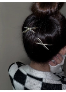 Detailed view of two silver X-shaped hair clips with sparkling rhinestones on model