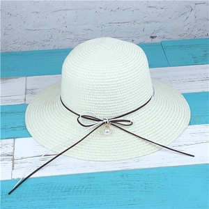 Detail of summer straw hat featuring woven texture with bow tie and pearl pendant