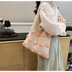 Detail view of a beige knitted shoulder bag with colorful floral patterns on a model