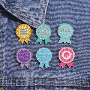 Detailed close-up of six colorful enamel award pins on blue denim fabric background