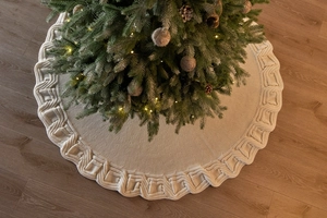 Close-up of thick knit cream white Christmas tree skirt on dark wood floor texture