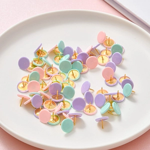 Pastel macaron push pins with golden tips in a white ceramic dish for office stationery