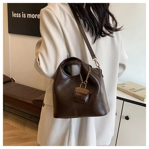 Model wearing dark brown leather bucket bag with gold chain detail and lock charm