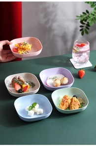 Top view of five colorful square fruit plates with food on a dark green table
