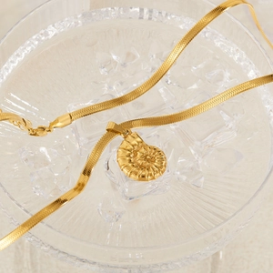 Macro shot of gold snake chain with a conch shell pendant on clear ice cubes