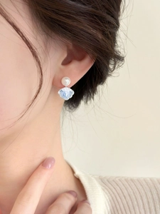 Detailed view of silver needle pearl earrings with blue textured floral petal pendants