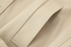 Detailed close-up of stitching on a beige trench coat pocket with twill fabric texture