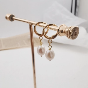 Close-up of elegant gold hoop earrings with white teardrop pearls on a display stand