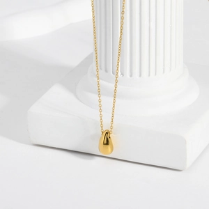 Close-up of a gold waterdrop pendant necklace hanging elegantly on a white Roman column