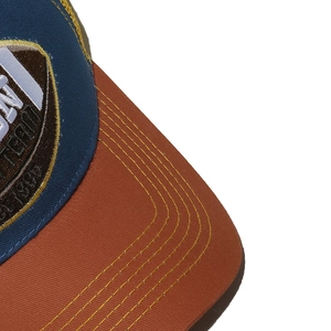Close-up of baseball cap stitching and mountain embroidery badge on blue fabric