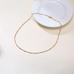 Close-up of golden satellite chain necklace with tiny beads on a ceramic plate