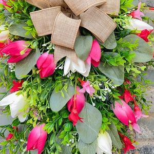 Illuminated Christmas wreath with pink tulips, greenery leaves and burlap bow on stone wall