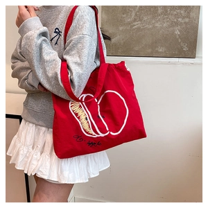 Red canvas tote bag with hand-drawn apple print worn by a model in a minimalist setting