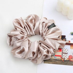 Detailed view of champagne satin scrunchie with silky texture and branding tag