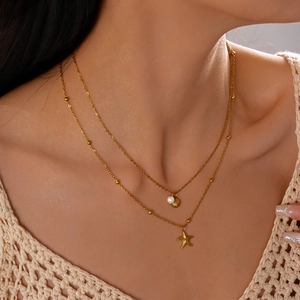 Detail of layered gold necklace with starfish, shell charms and faux pearls on model