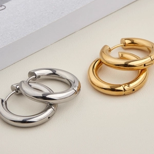 Minimalist gold and silver titanium steel hoop earrings with polished finish on beige background