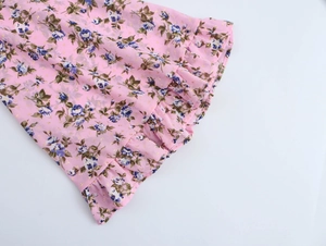 Dettaglio del tessuto in chiffon rosa con stampa floreale, volant e fiori blu