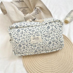 Quilted floral makeup bag with blue begonia pattern and fabric logo on linen surface