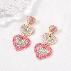 Vintage heart earrings with pink pearls and clear crystals on a textured white surface
