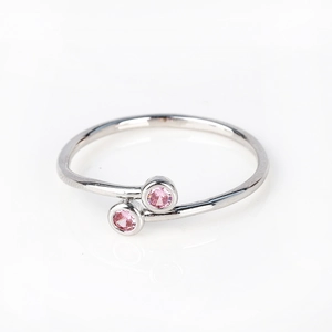 Detail of silver bypass ring featuring two round pink zircon stones on a white background