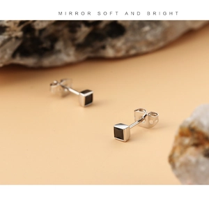 Macro shot of silver stud earrings with square black zircon stones on rock background