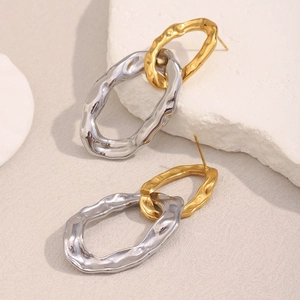 Close-up of hammered two-tone 18K gold plated stainless steel hoop earrings on beige texture
