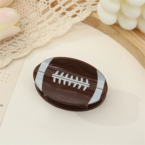 American football claw clip in brown acrylic with white stitch pattern on a warm background