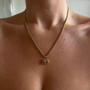 Close-up of a 99 year number pendant on a gold twisted rope chain necklace worn by a model
