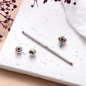 Close-up of a silver industrial barbell with a crown-set red gemstone on a textured background