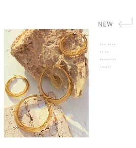 Detailed macro of gold-plated hoop earrings with unique coil textures on stone background