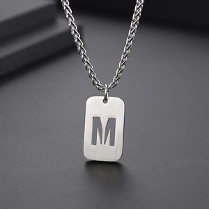 Détail macro du pendentif rectangulaire argenté avec lettre M évidée brossée