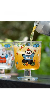 Détail d'un verre à motif panda versant un jus coloré dans un grand verre élégant