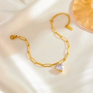 Gold heart zircon bracelet with paperclip chain on white silk background