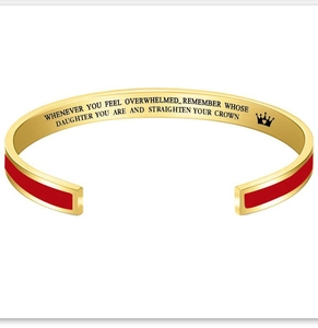 Macro view of golden cuff bracelet featuring red enamel and engraved inspirational quote inside