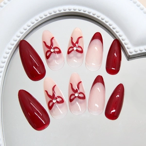 Elegant wine red cat-eye nails with bow patterns and rhinestones on mirrored display
