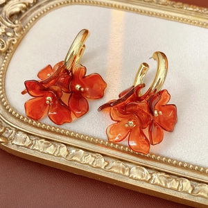 Detail view of retro gold C-shaped earrings with translucent orange flower petals