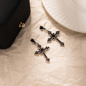 Détail de boucles d'oreilles croix argentées avec cristaux noirs sur papier