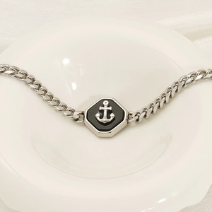 Polished silver Cuban link bracelet with anchor pendant displayed in a white ceramic bowl