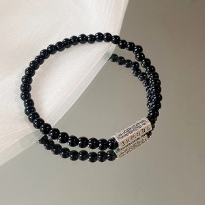 Makroaufnahme schwarzer Obsidianperlen und Silberhülse mit gravierten Sanskrit-Symbolen