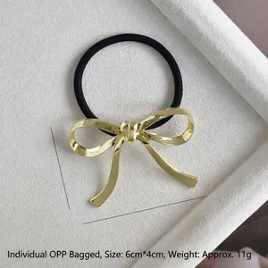 Close-up of a gold metal bow hair tie with dimensions 6cm by 4cm on a white tray