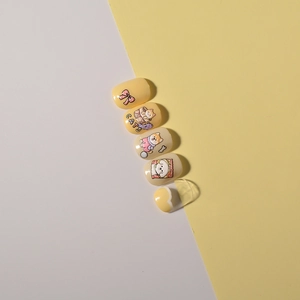 Detail of cute handmade press-on nails featuring cat, dog, and bow patterns on yellow base