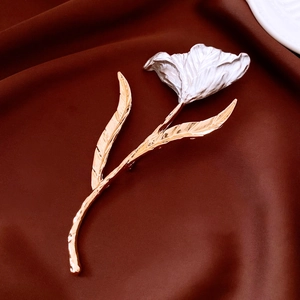 Détail d'une broche tulipe avec pétales argentés et tige dorée sur tissu brun