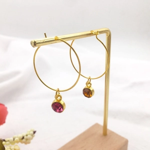 Gold hoop earrings with round gemstone pendants on a wooden jewelry display stand