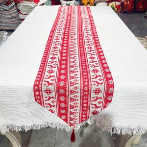 Christmas table runner with reindeer and snowflake patterns and red tassels on white fabric