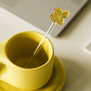 Amber clover heat-resistant glass coffee stirrer placed in a yellow cup on a desk