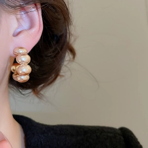 Close-up of elegant C-shaped gold-plated hoop earrings with pearls worn by a model
